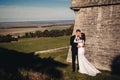 Newlywed couple posing near old castle wall, fairytale wedding at ancient castle outdoors, bride and groom hugging near fortress Royalty Free Stock Photo