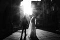 Newlywed couple standing in street, Beautiful blonde bride in white wedding dress posing near handsome groom in sunny french