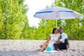 Millennial couple sitting by the beach under umbrella while kissing Royalty Free Stock Photo