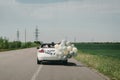 A newlywed wedding couple is driving a convertible retro car with balloons on a country straight road for their honeymoon. Way Royalty Free Stock Photo