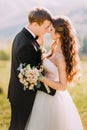 Newlywed young bride and groom with flower bouquet rubbing noses outdoors Royalty Free Stock Photo