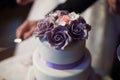 Newlyweds carving delicious white wedding cake with purple roses