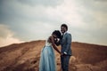 Newlyweds hold hands, laugh and stand against beautiful landscape.