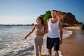 Romantic couple strolls on beach at sunset. Newlyweds on honeymoon enjoy sea, sand near cliffs. Man in tank top, woman Royalty Free Stock Photo