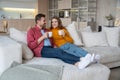 Newlyweds hugging lie on huge home sofa. Young couple happily drinks coffee enjoying weekend time. Royalty Free Stock Photo