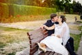 Newlyweds kissing at bench in park.