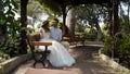 Newlyweds sitting on bench in green garden. Action. Beautiful young couple are sitting and chatting on bench in Royalty Free Stock Photo