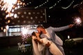 newlyweds with sparklers in night park with garlands in trees. ending to wedding