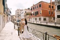 Italy wedding in Venice. Newlyweds stand embracing on the banks of the Venice Canal. The groom hugs the bride by the