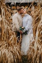 Newlyweds stand near dry grass and kiss