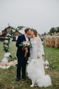 Newlyweds stand near wedding arch and kiss next to dog