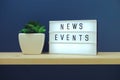 News Events word in light box on blue and wooden shelves background