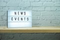 News Events word in light box on brick wall and wooden shelves background