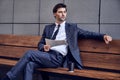 Daily news. Full length of a pleasant smiling businessman reading a newspaper with coffee while sitting on the bench Royalty Free Stock Photo