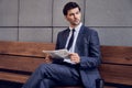 Daily news. Full length of a pleasant smiling businessman reading a newspaper with coffee while sitting on the bench Royalty Free Stock Photo