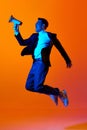 News. Full-length portrait of young man in stylish clothes jumping and shouting in megaphone against orange studio