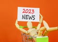 2023 News symbol. White paper with words 2023 News, human model in shopcart. Beautiful orange table orange background. Business Royalty Free Stock Photo