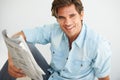 Newspaper, happy and young man reading information and relaxing on a weekend morning at home. Smile, smart and handsome