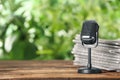 Newspapers and vintage microphone on wooden table against blurred green background, space for text Royalty Free Stock Photo