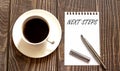 NEXT STEPS - white paper with pen and coffee on wooden background