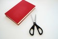 Next to the book which has a red cover there are scissors Royalty Free Stock Photo
