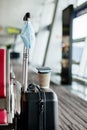 Next to the seats in an empty airport is a suitcase, on it is a glass of coffee, hanging a medical protective mask