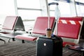 Next to the seats in an empty airport is a suitcase, on it is a glass of coffee, hanging a medical protective mask