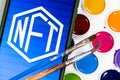 NFT symbol on the background of watercolors and two paintbrushes