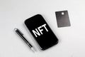 NFT word on smartphone with credit card and pen