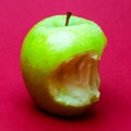 Nibbled wet green apple against red background 2