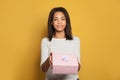 Nice african american woman holding pink gift box on colorful yellow background