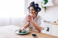 Nice attractive beautiful young woman in kitchen. Hold cup in hands and dream. Eyes closed. Pancakes on plate. Phone on Royalty Free Stock Photo