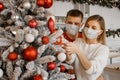 Nice attractive couple wearing face protective medical mask are concentrated on decorating christmas tree at home Royalty Free Stock Photo