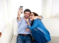 Nice attractive young couple sitting together in sofa couch taking selfie photo with mobile phone Royalty Free Stock Photo