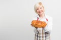 Nice and awesome picture of smiling grandma that baked a tasty pie. She holds the pie in ger hands and want it to share