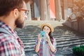 Nice and beautfiul young female tourist stand at steps and hold blue camera. She takes picture of her boyfriend and look