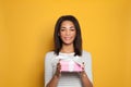 Nice black woman opening pink gift box with white silky ribbon on bright yellow background