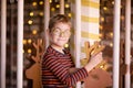 Nice blonde boy with glasses on the new year carousel with wooden deer and bright lights