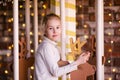 Nice blonde girl on the new year carousel with wooden deer and bright lights