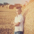 The nice boy in the field of near stack of straw at sunset