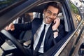 Nice business talk. Handsome young businessman talking on his smart phone and smiling while sitting on the front seat