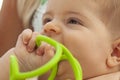 Nice closeup portrait of cute blond baby with brown eyes biting in a green plastic teether. Close up image