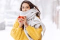 Nice dark-haired girl in a yellow sweater and a white scarf standing with a red mug on a snowy street on a winter day Royalty Free Stock Photo