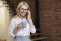 Nice day. Middle aged business woman with blonde hair and glasses holding a cup of coffee or tea while talking on her Royalty Free Stock Photo