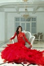 Nice fashionable woman wearing red evening gown sitting on armchair in luxurious palace interior Royalty Free Stock Photo