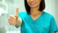 Nice female stomatologist smiling at camera, showing thumbs-up, health care