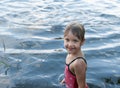A nice four-year old girl stands smiling and laughing in the open water.