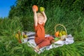 nice and funny fair-haired kid holds an orange over his head, basket with fruits on green grass Royalty Free Stock Photo