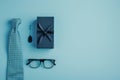 A nice gift box with a necktie and glasses on pastel blue background. Flat lay, top view. Copy space on the bottom. Royalty Free Stock Photo