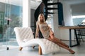 A nice girl with a beautiful figure in a short shiny dress rests on a white stylish sofa in the studio. Portrait of an Royalty Free Stock Photo